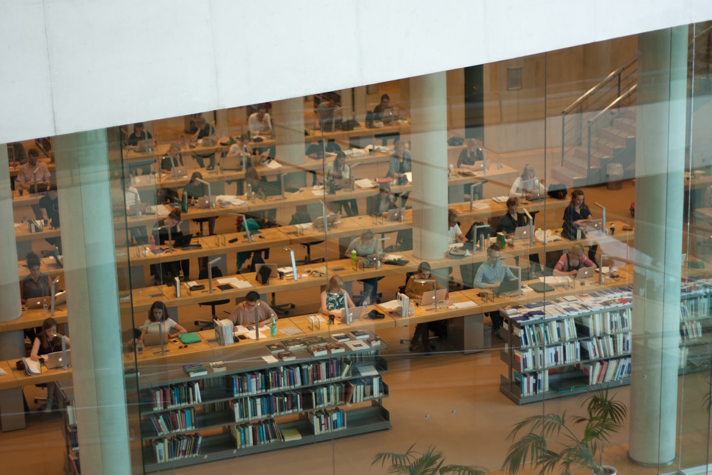 Students work on laptops and read at desks in a library.