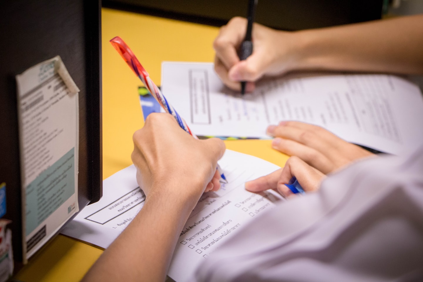 Two students writing on paper forms at a desk.